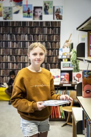 Stedelijk buitengewoon onderwijs: lachend meisje staat met boek in de bib van Leerexpert Jozef Van Poppelstraat