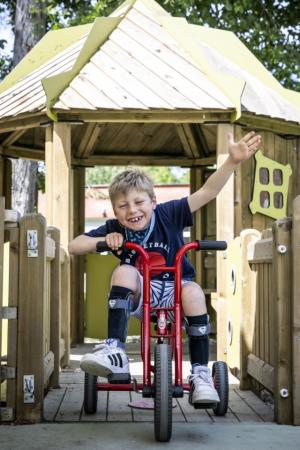 Stedelijk buitengewoon onderwijs_lachende jongen rijdt op driewieler op de speelplaats van Leerexpert Kokoen